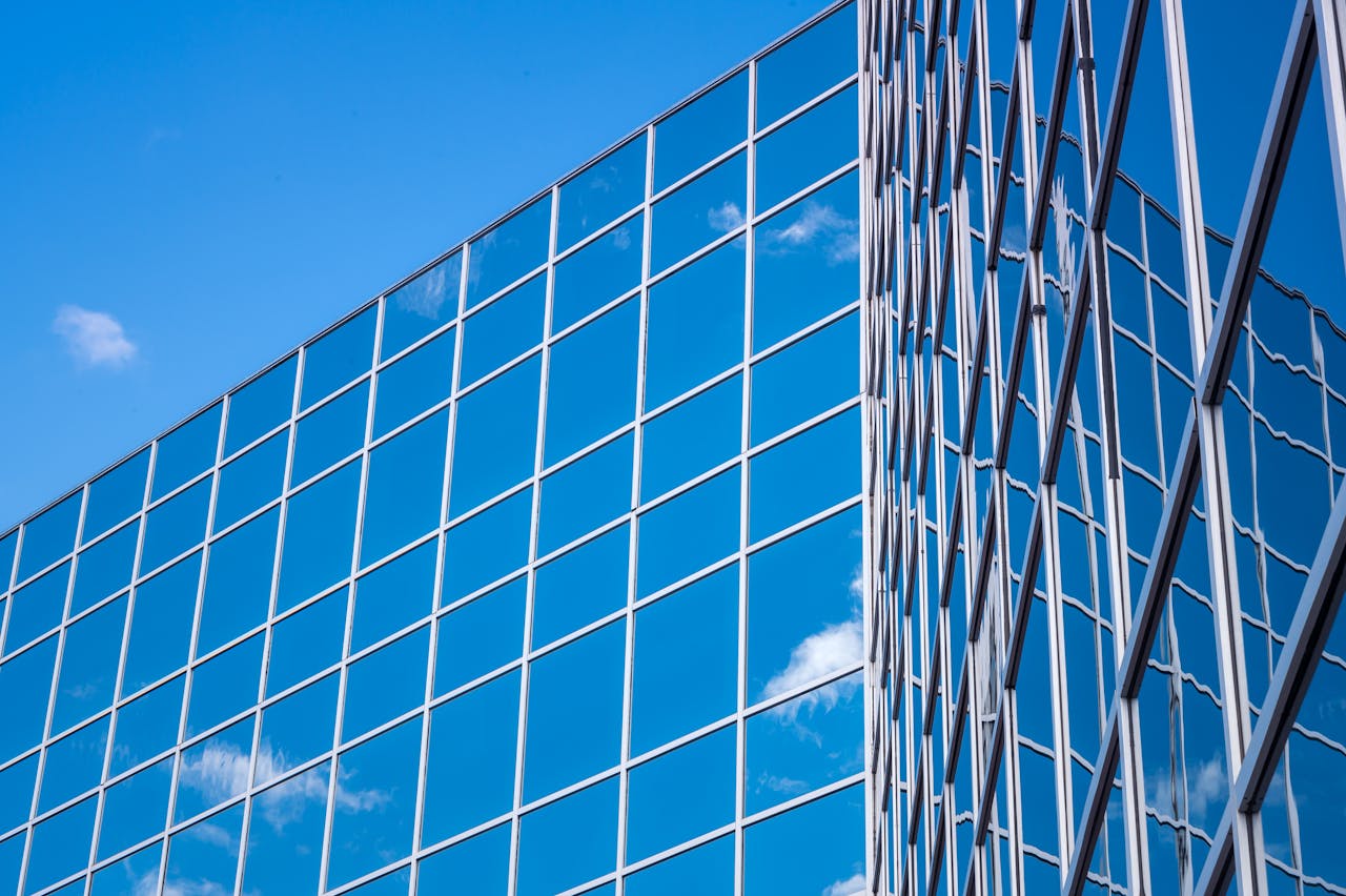 Contemporary glass building with a reflective facade showing a blue sky and clouds.